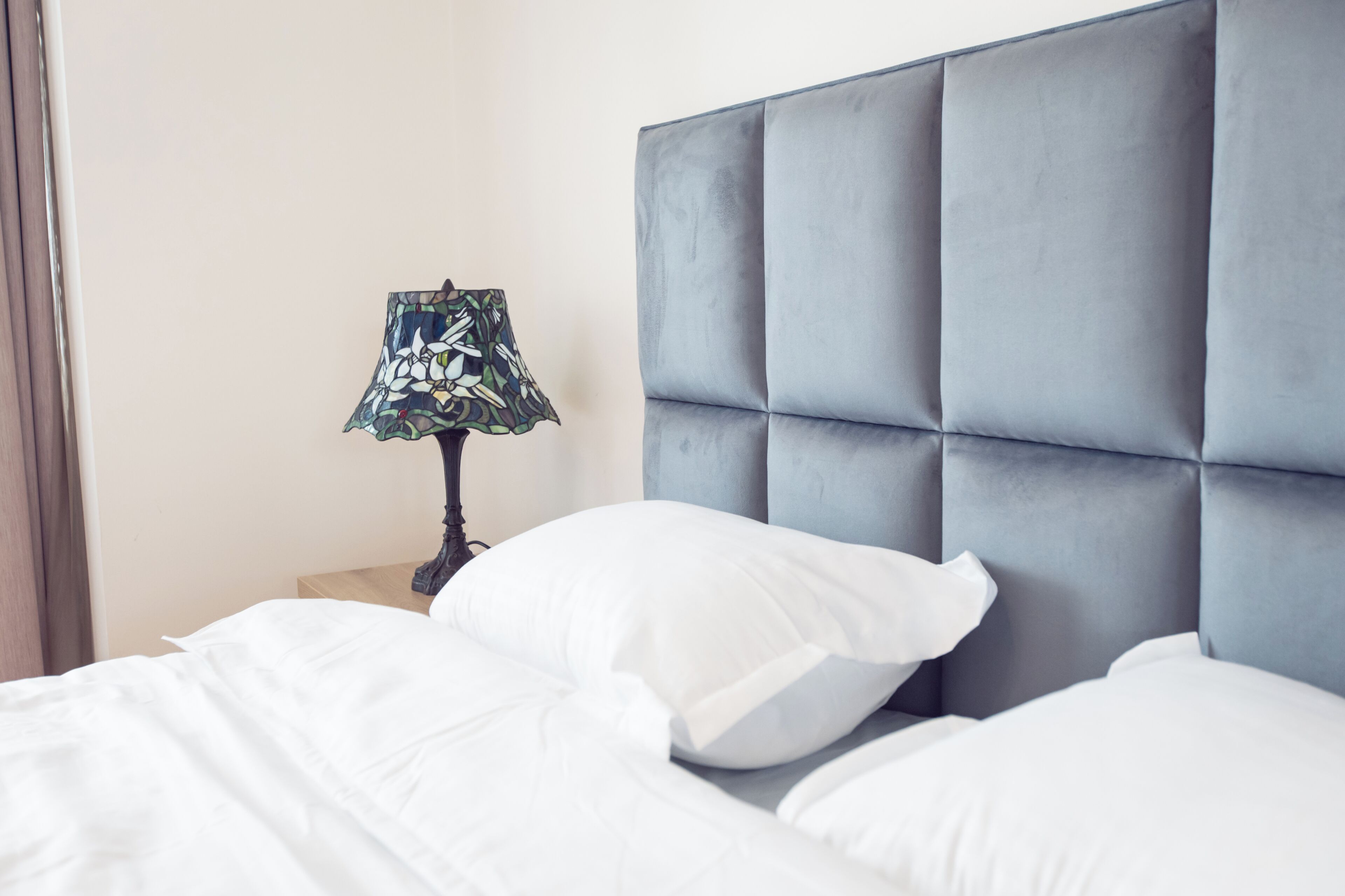 Een net opgemaakt bed met witte beddengoed en een grijs hoofdbord.