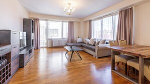 Una sala de estar moderna con una mesa de comedor de madera, un conjunto de sofás, un televisor y una estantería para vinos.