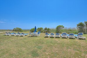 Un espacio con césped, varias sillas de descanso y una mesa, probablemente para comer al aire libre o relajarse.