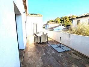 A patio with a table and chairs, a tiled floor, and a view of neighboring buildings and trees. - Appt 3 stars, view on bassin de Thau Terr 30 m² Pets accepted (Mèze)