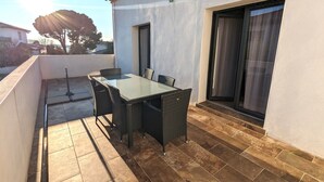 A patio with a glass-top table and wicker chairs, a tiled floor, and a building with a white exterior and a window with curtains. - Appt 3 stars, view on bassin de Thau Terr 30 m² Pets accepted (Mèze)