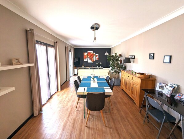 A modern living room with a dining area, wooden flooring, and a large window with curtains. - Appt 3 stars, view on bassin de Thau Terr 30 m² Pets accepted (Mèze)