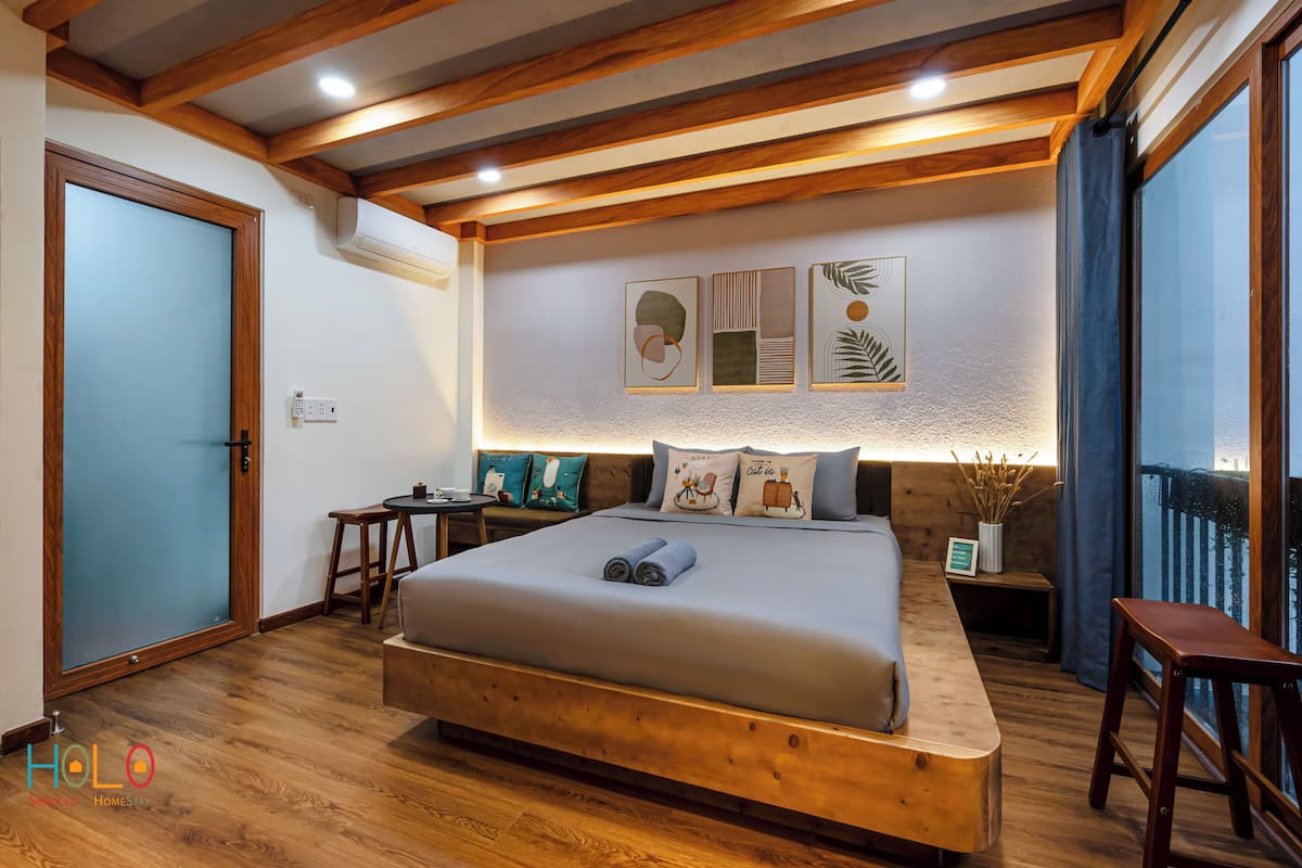 A modern bedroom with a wooden bed, a small desk, and a balcony with a view.