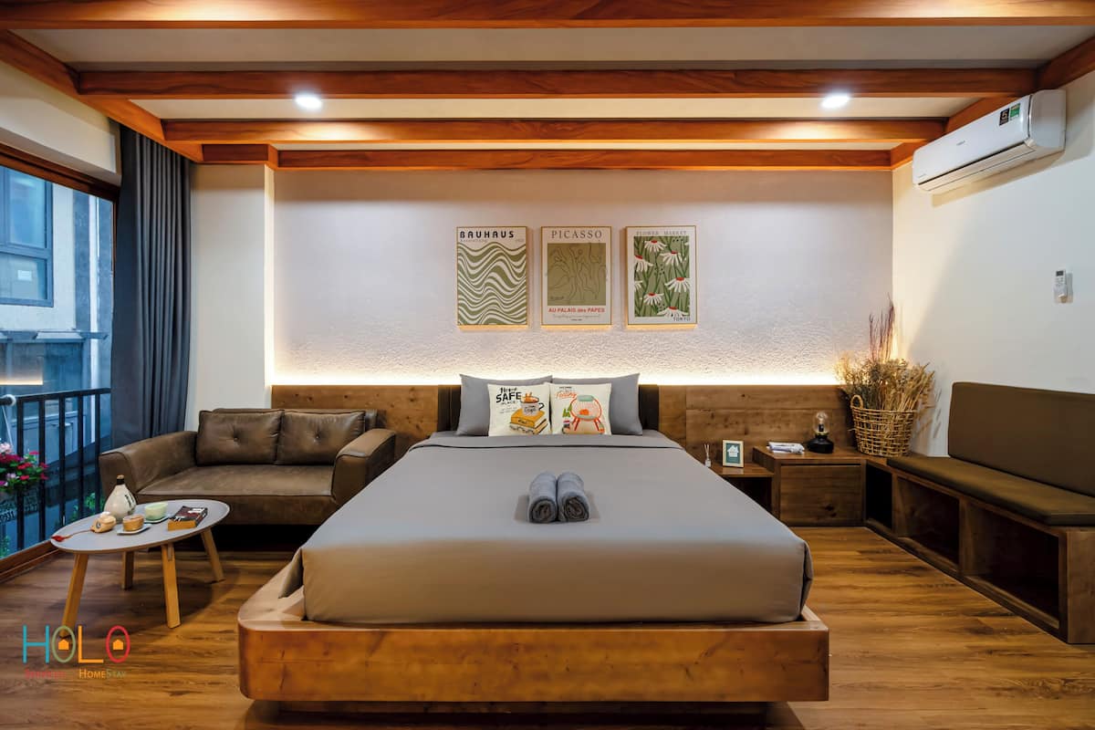 A modern hotel room with a large bed, a sofa, a small table, and a balcony with a view.