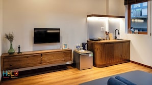 A modern hotel room with a flat-screen TV, wooden furniture, a small kitchenette, and a large window.