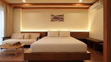 Habitación de hotel con una cama grande, un sofá, una mesa de centro de madera y un aire acondicionado instalado en la pared.