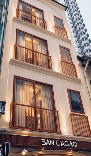 Un edificio con diversi balconi, un cartello con la scritta 'BAN CACAÓ' e un moderno grattacielo sullo sfondo.