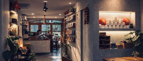 A cozy cafe interior with a central counter, bookshelves, and a display of cups and saucers.