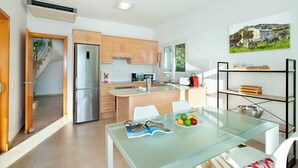 Une cuisine moderne avec des meubles en bois, un réfrigérateur en acier inoxydable et une table à manger en verre, accompagnée de chaises.