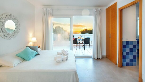 Une chambre d’hôtel avec un lit, une vue sur le coucher de soleil depuis le balcon et un coin repas avec des chaises et une table.