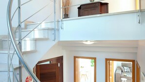 Un intérieur moderne avec un escalier en colimaçon, une porte en bois et une vue sur un espace de vie comprenant un canapé et une petite table.