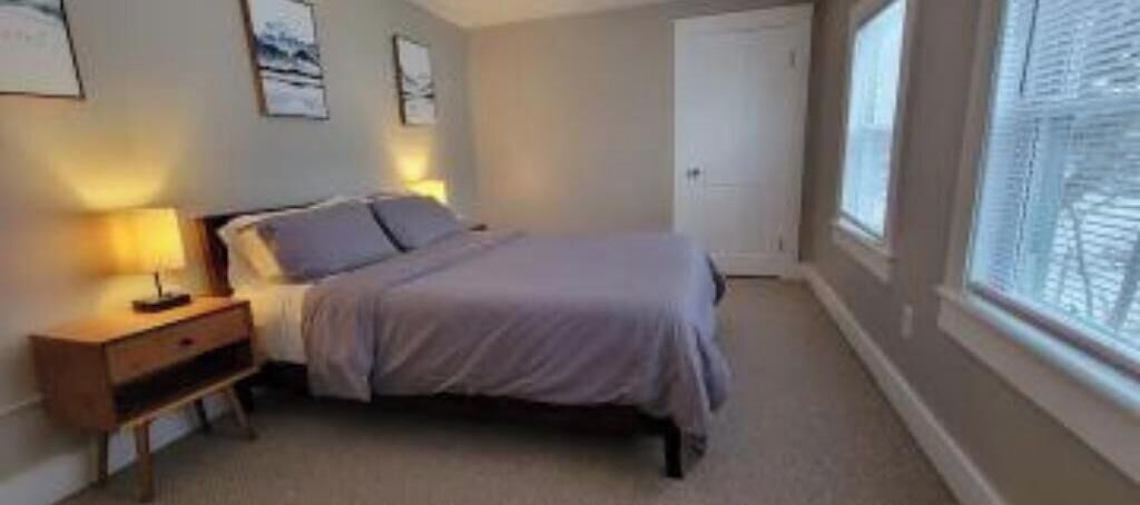 Quarto com cama, mesa de cabeceira e janela.