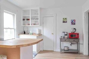 A compact kitchen with white cabinetry, a wooden countertop, a red microwave, and a small table with a kettle and a pot.