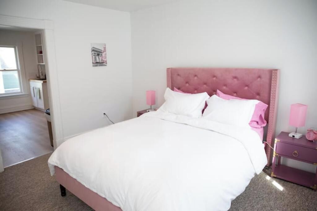 A bedroom with a pink tufted headboard, white bedding, and pink bedside lamps.