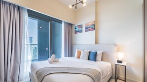 Hotellihuone, jossa on sänky, yöpöytä, lamppu ja taideteos seinällä.