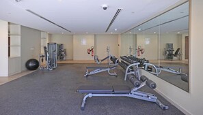 A gym with various exercise equipment, a mirrored wall, and a fire extinguisher on the wall. - Enticing 2BR Apartment in Reva Residences, Business Bay by Deluxe Holiday Homes (Dubai)