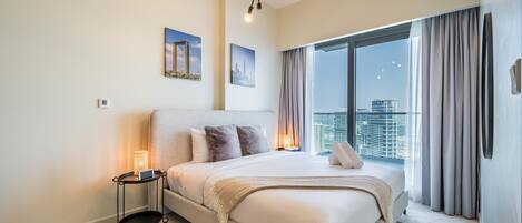 Une chambre moderne avec un grand lit, une table de chevet avec une lampe et une vue sur la ville à travers de grandes fenêtres.
