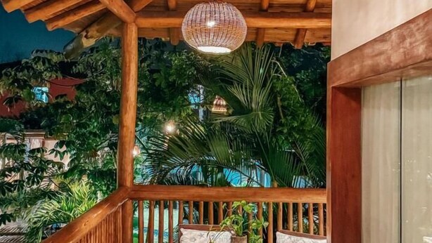 Een houten balkon met rieten hanglampen, twee comfortabele stoelen en een kleine ronde tafel met een plant.