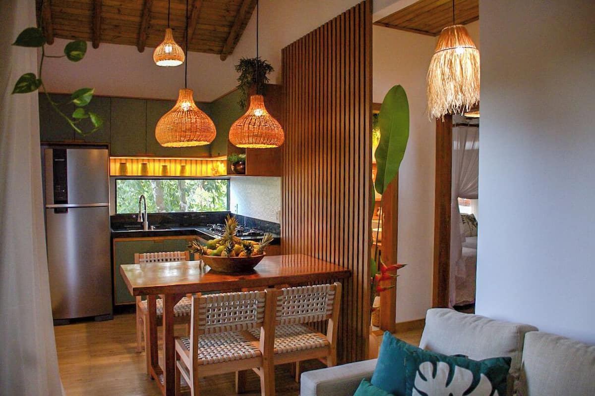 A modern kitchen with a wooden dining table, wicker chairs, and a fruit bowl.