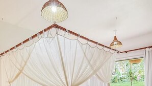 Een ruime slaapkamer met hemelbed, houten vloer en uitzicht op een tuin.