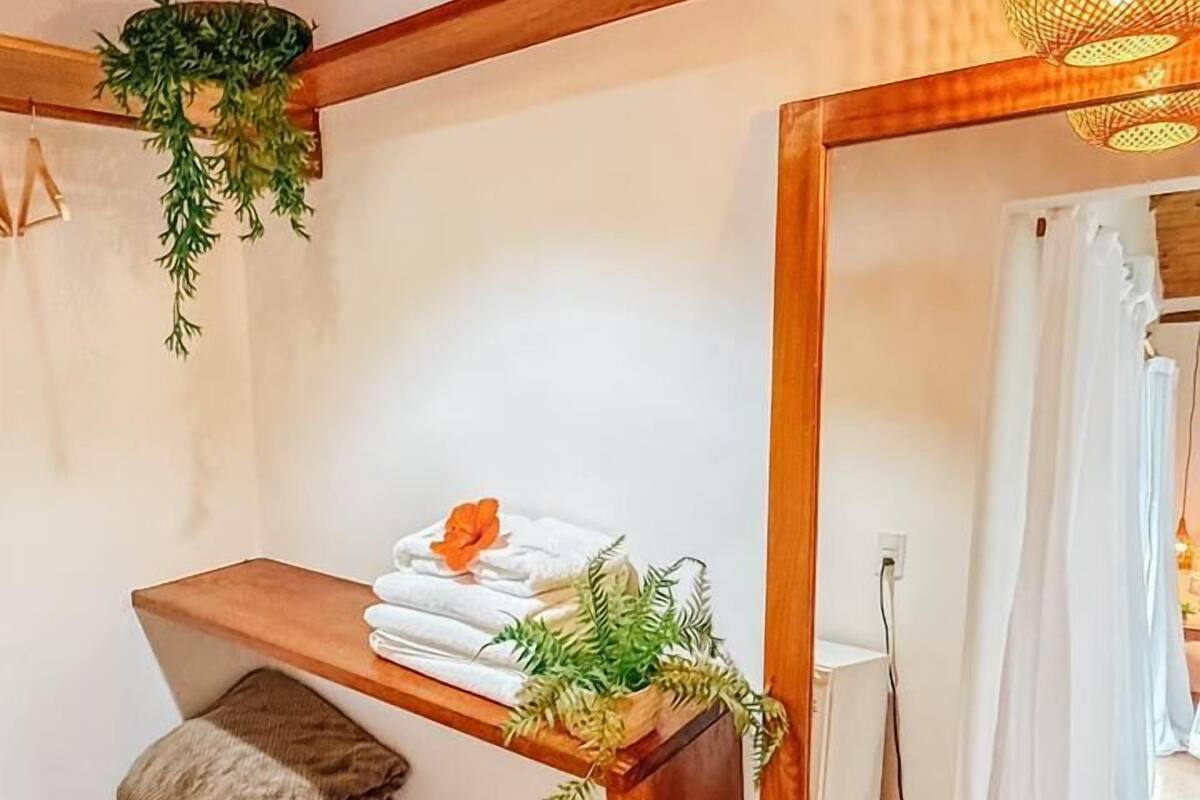A cozy room with wooden beams, a hanging light fixture, a mirror, and a shelf with towels and plants.