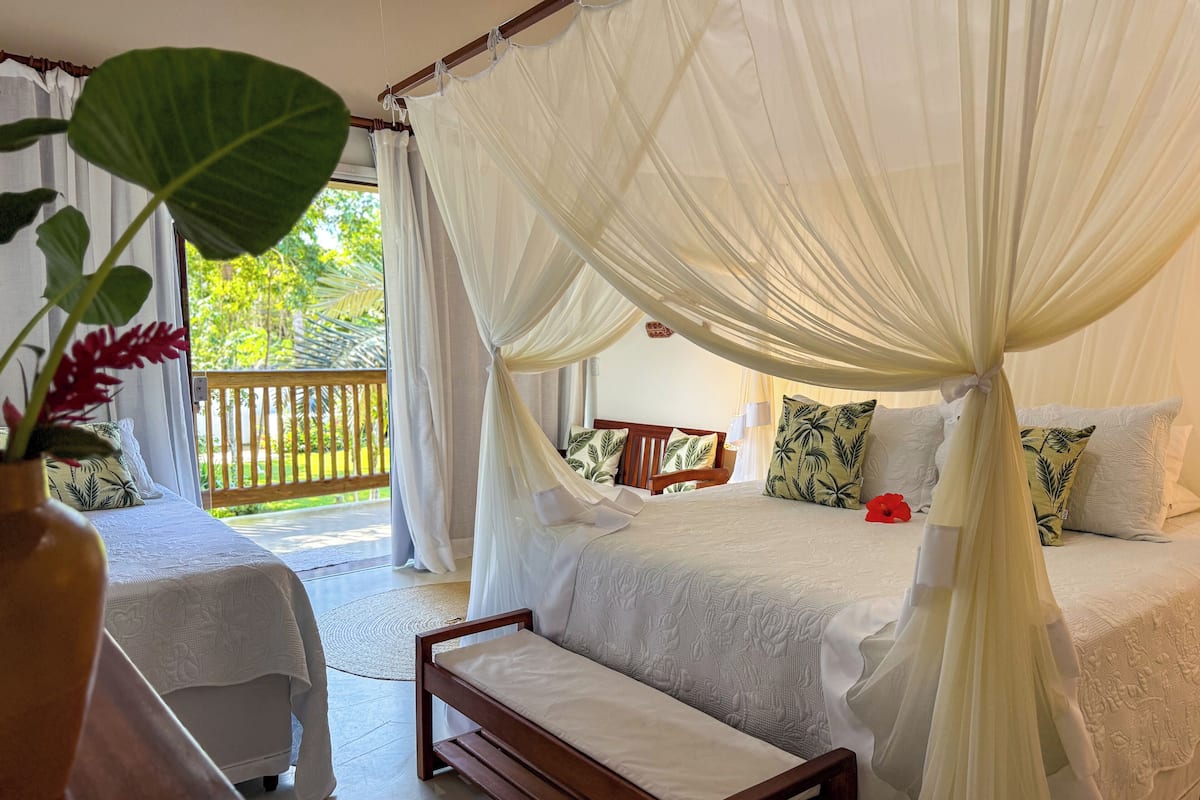 A bedroom with a canopy bed, a bench, and a view of the outdoors.