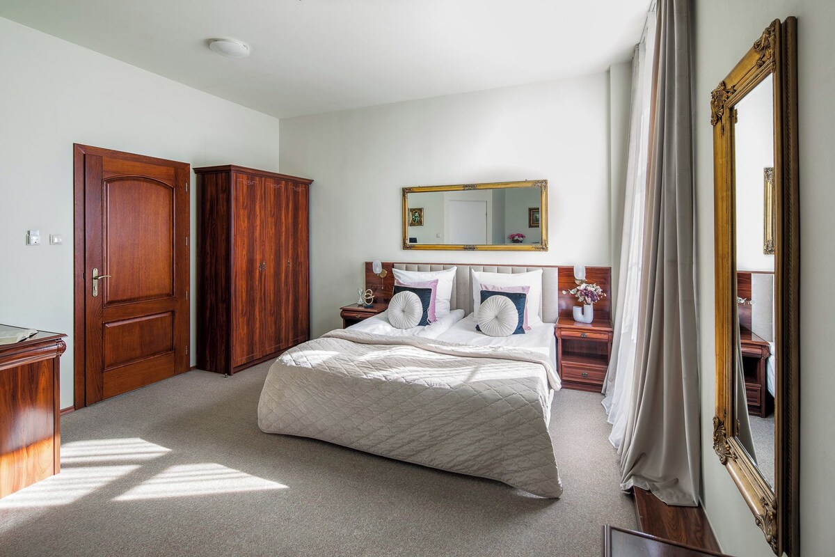 A bedroom with a bed, a wardrobe, a nightstand, a mirror, and a door.
