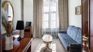 Una sala de estar con sofá, una mesa, una lámpara, un espejo y una ventana con cortinas.