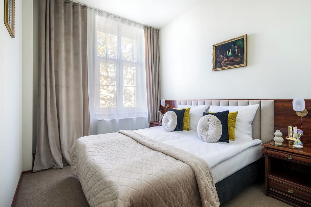 A neatly made bed with a quilt, a bedside table with a lamp, and a painting on the wall.