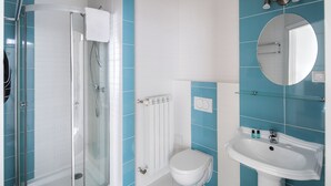 Un baño con ducha de vidrio, inodoro blanco y lavamanos pedestal con espejo arriba.