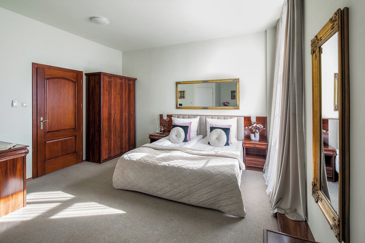 A bedroom with a large bed, wooden wardrobe, a nightstand with a lamp, and a mirror.