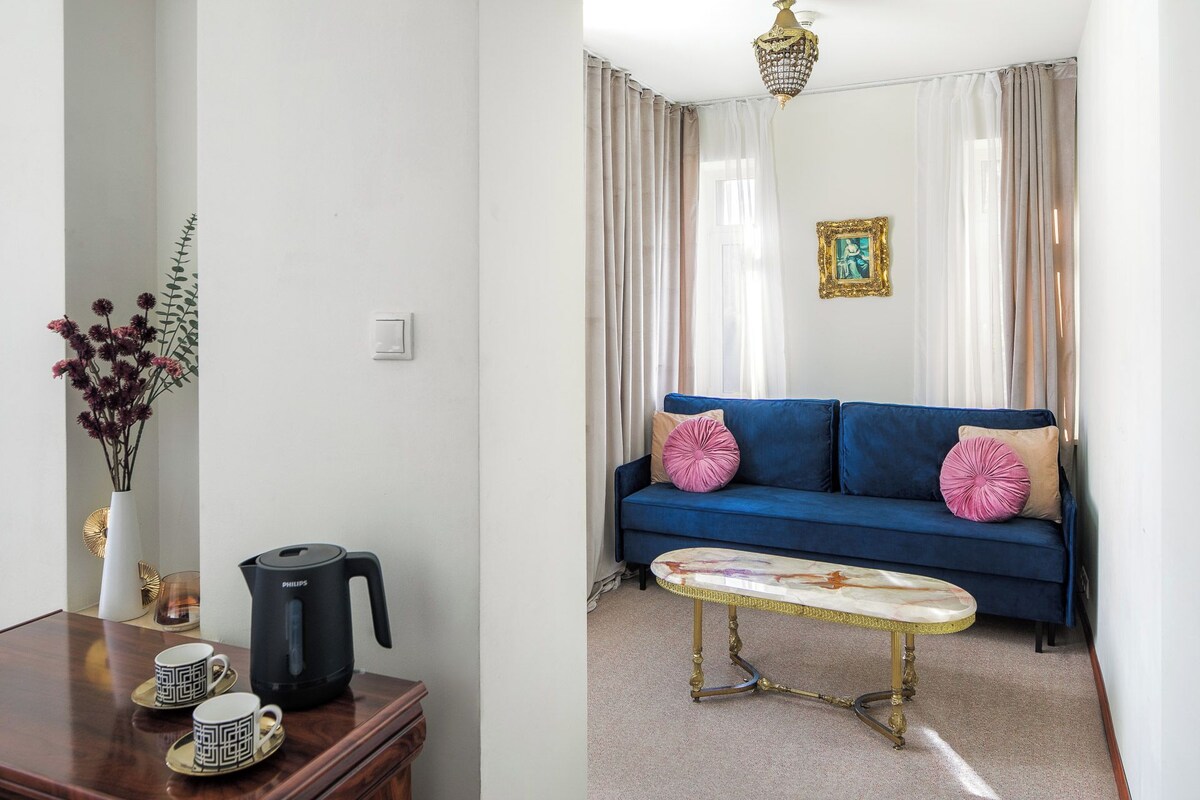 A living room with a blue sofa, a coffee table, a vase with flowers, a coffee maker, and a picture frame on the wall.