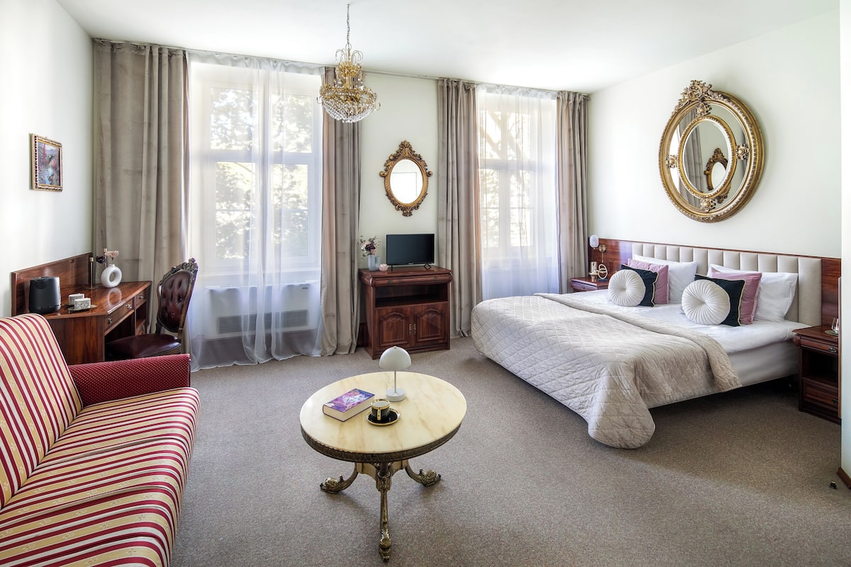A hotel room with a bed, a sofa, a TV, a table, and curtains.