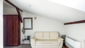 Una habitación con sofá color beige, un armario de madera, una mesita con un florero, un espejo y un calentador de pared.