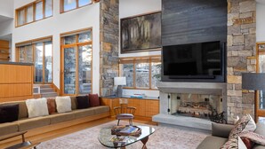 A spacious living room with a stone fireplace, a large flat-screen TV, and a comfortable seating area with a sofa and armchairs. - Gray Mill House-Curate Telluride-New Remodel, Hot Tub, Grill, Views, Lux Home (Mountain Village)