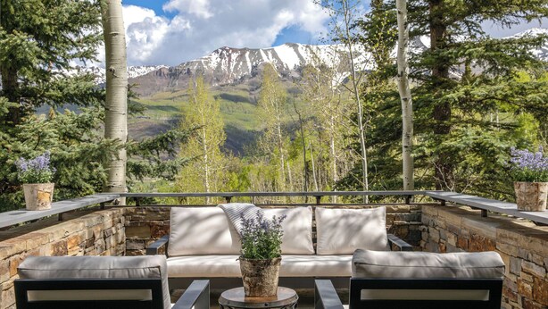 A patio with a sofa and chairs, a stone wall, and a view of a mountain range. - Gray Mill House-Curate Telluride-New Remodel, Hot Tub, Grill, Views, Lux Home (Mountain Village)