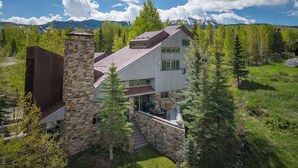 A modern house with a stone chimney, large windows, and a view of mountains. - Gray Mill House-Curate Telluride-New Remodel, Hot Tub, Grill, Views, Lux Home (Mountain Village)