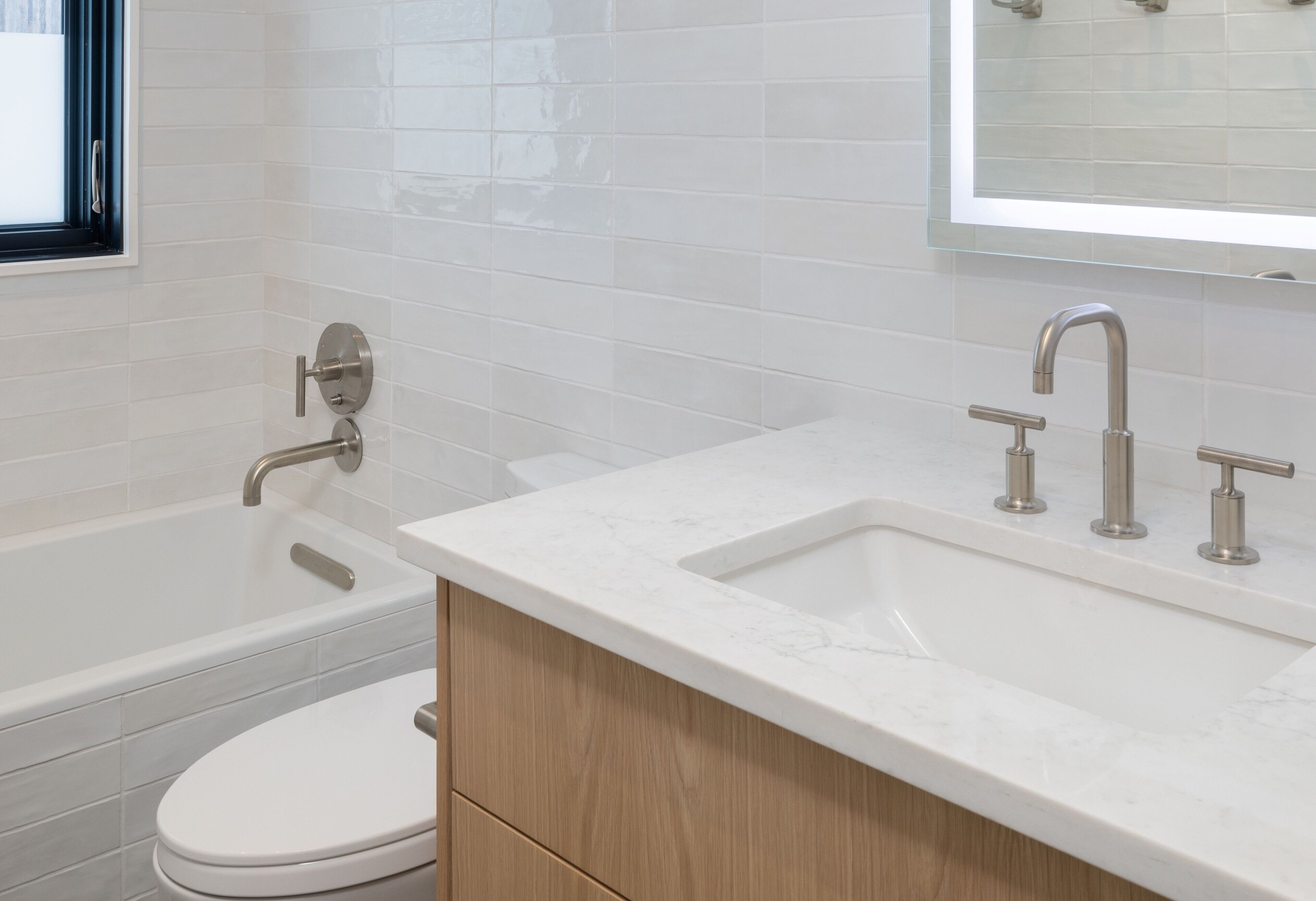 A modern bathroom with a bathtub, a toilet, and a sink with a mirror above.