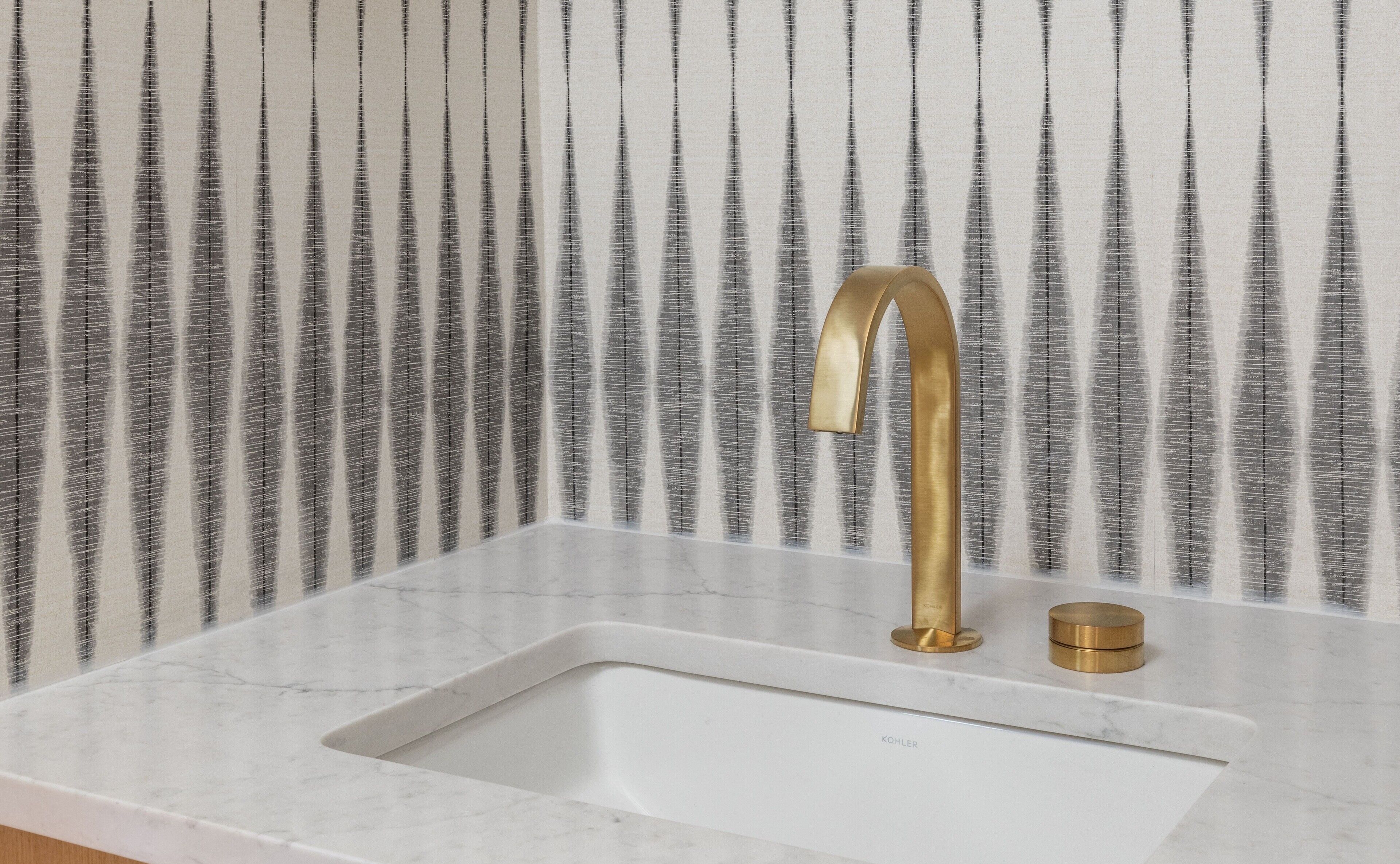 Un lavabo con grifo dorado y detalles en latón, sobre un fondo de papel tapiz a rayas.