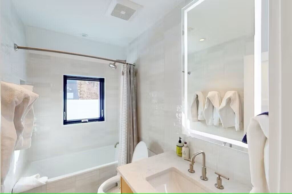 A modern bathroom with a bathtub, a large mirror, and a window.