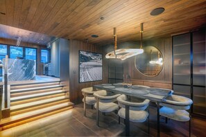 Un espace repas moderne avec un plafond en bois, une grande table entourée de chaises et une vue sur un paysage enneigé par la fenêtre.