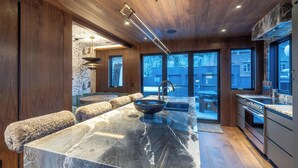 A modern kitchen with a marble countertop, wooden ceiling, and large windows. - New Penthouse, Center of Town, Sauna, Deck, Fireplace, Views, Parking, Ski Room (Telluride)