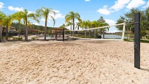 Un terrain de beach-volley avec un filet, des palmiers et un bâtiment en arrière-plan.