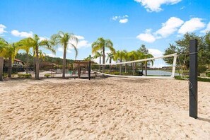 A beach volleyball court with a net, palm trees, and a building in the background. - Beautiful 12Bed/11.5Bath House  At Bella Vida (Kissimmee)