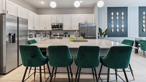 Une cuisine moderne avec des meubles blancs, des appareils en acier inoxydable et un îlot central agrémenté de chaises vertes.
