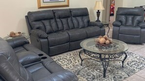 Un salon comprenant un canapé en cuir noir, un fauteuil assorti et une table basse en verre agrémentée d’objets décoratifs.
