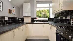 Een moderne keuken met een zwart aanrecht, witte kastjes, een ingebouwde kookplaat en een raam met uitzicht op groen.