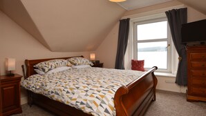 Een slaapkamer met een bed, nachtkastje, dressoir, televisie en een raam met gordijnen.