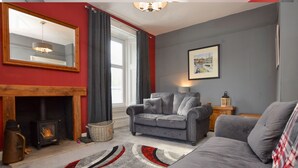 Un salon avec une cheminée, un canapé gris et un tapis aux motifs rouges et blancs.