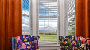 Une pièce comprenant deux fauteuils rembourrés aux motifs floraux colorés, une fenêtre avec des volets blancs et une vue sur un paysage.